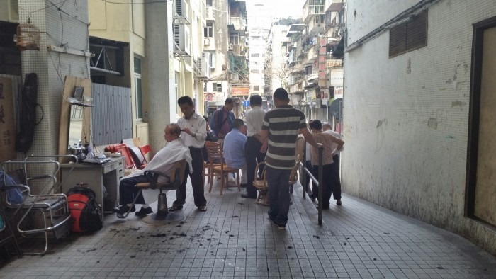 A barber snips away all day in an allyway off the main road in Macau