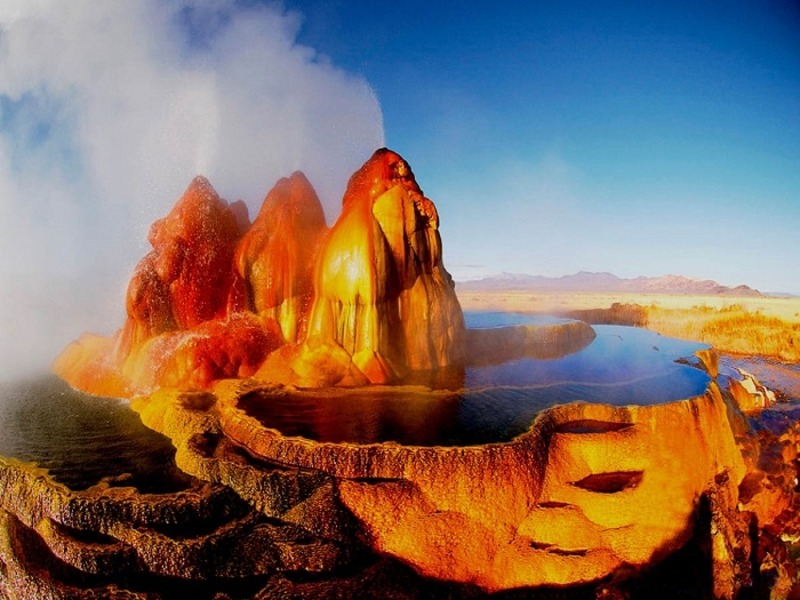 Shades of the World Series: Steam and water erupting out of Fly Geyser's orange, weird-looking mound, sided by a pool of water
