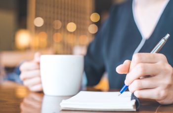 Business woman hand is on a notepad with a pen on a wooden desk in the office.